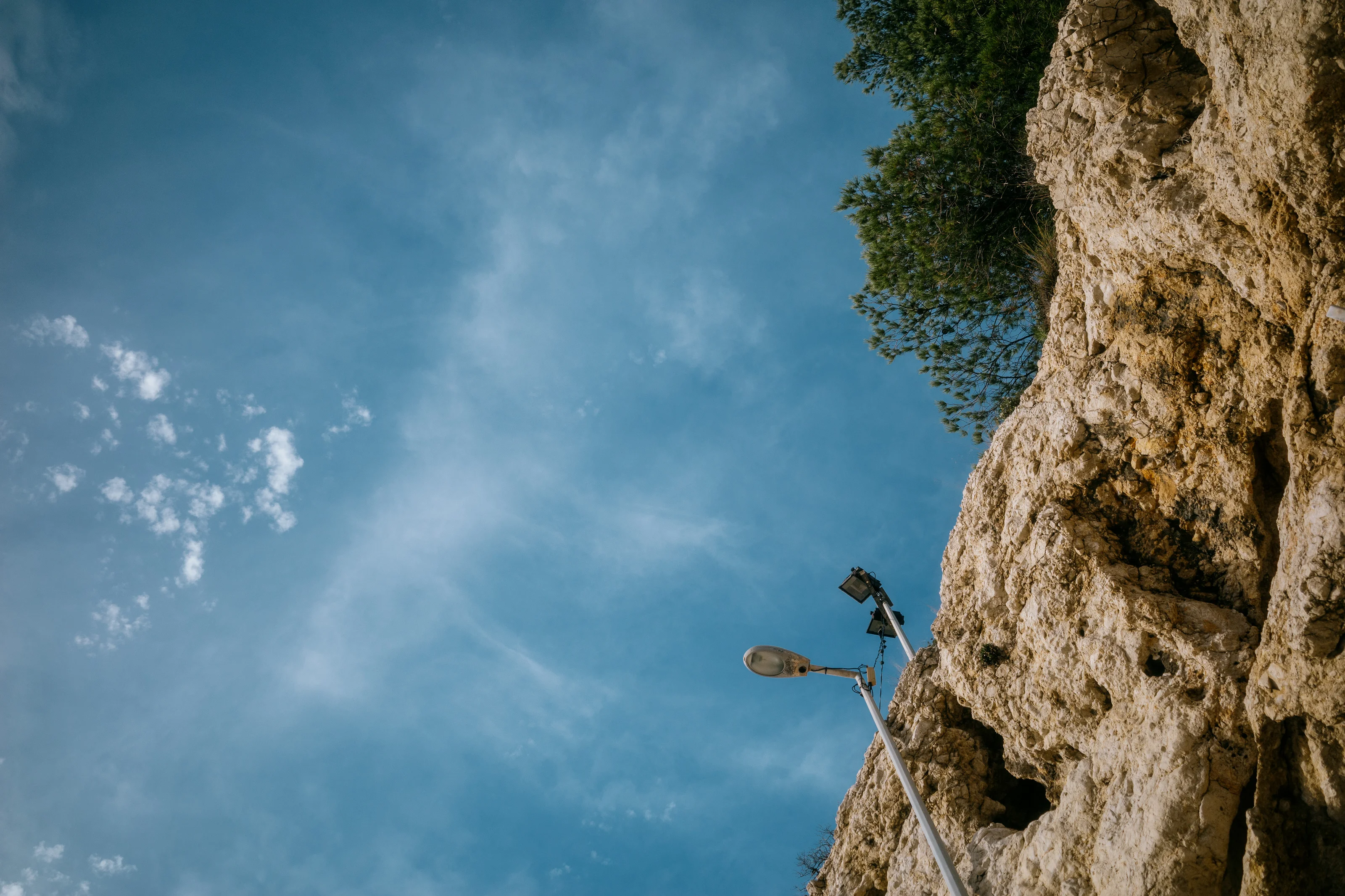 A streetlamp mounted on a rocky cliff against a blue sky with scattered clouds.