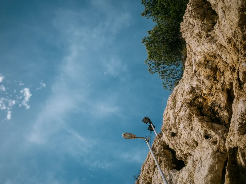A streetlamp mounted on a rocky cliff against a blue sky with scattered clouds.