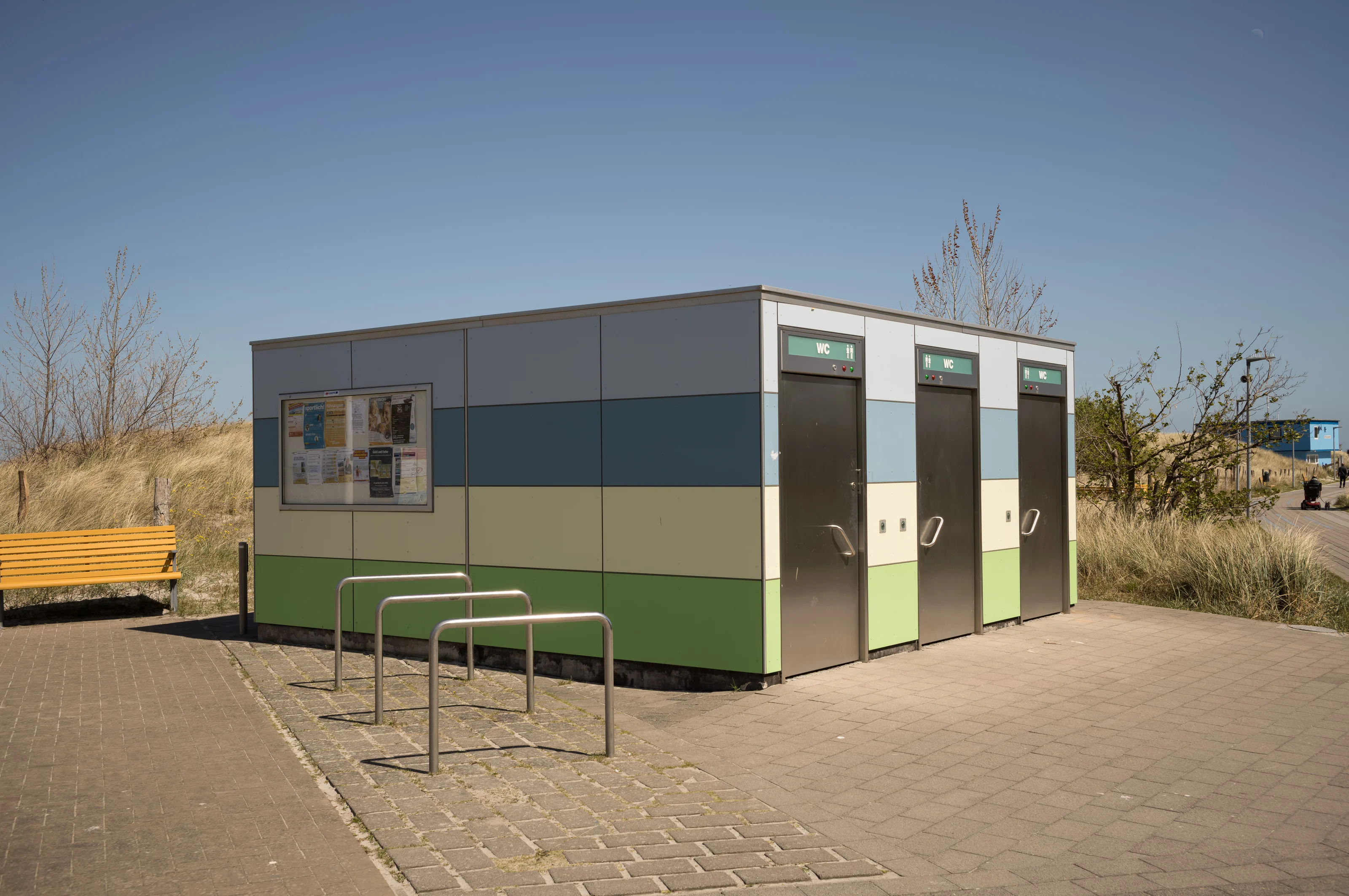 Colorful public restroom building with a bicycle rack and yellow bench in a park setting.