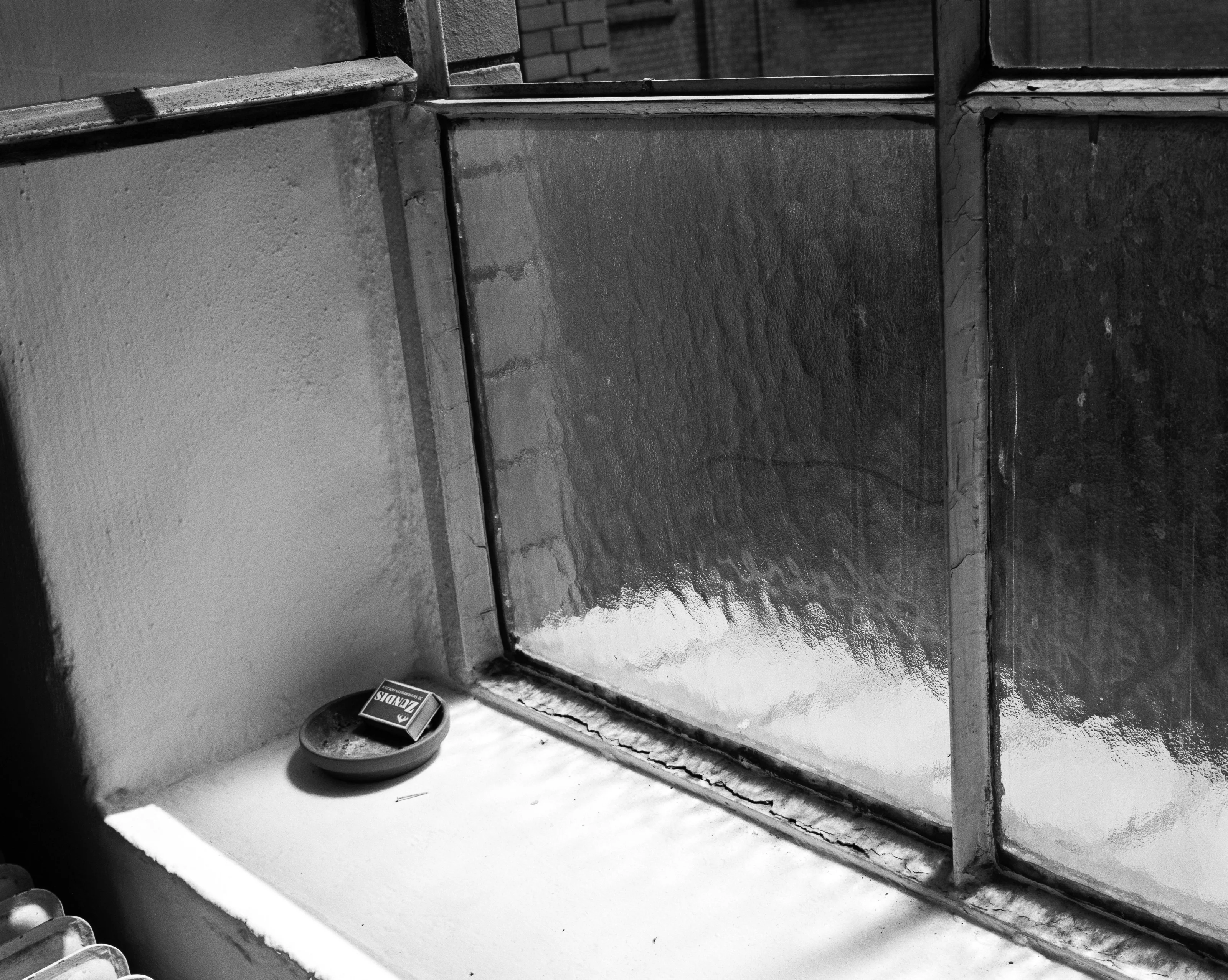 A small round tray with an empty cigarette box on a windowsill next to frosted glass windows.