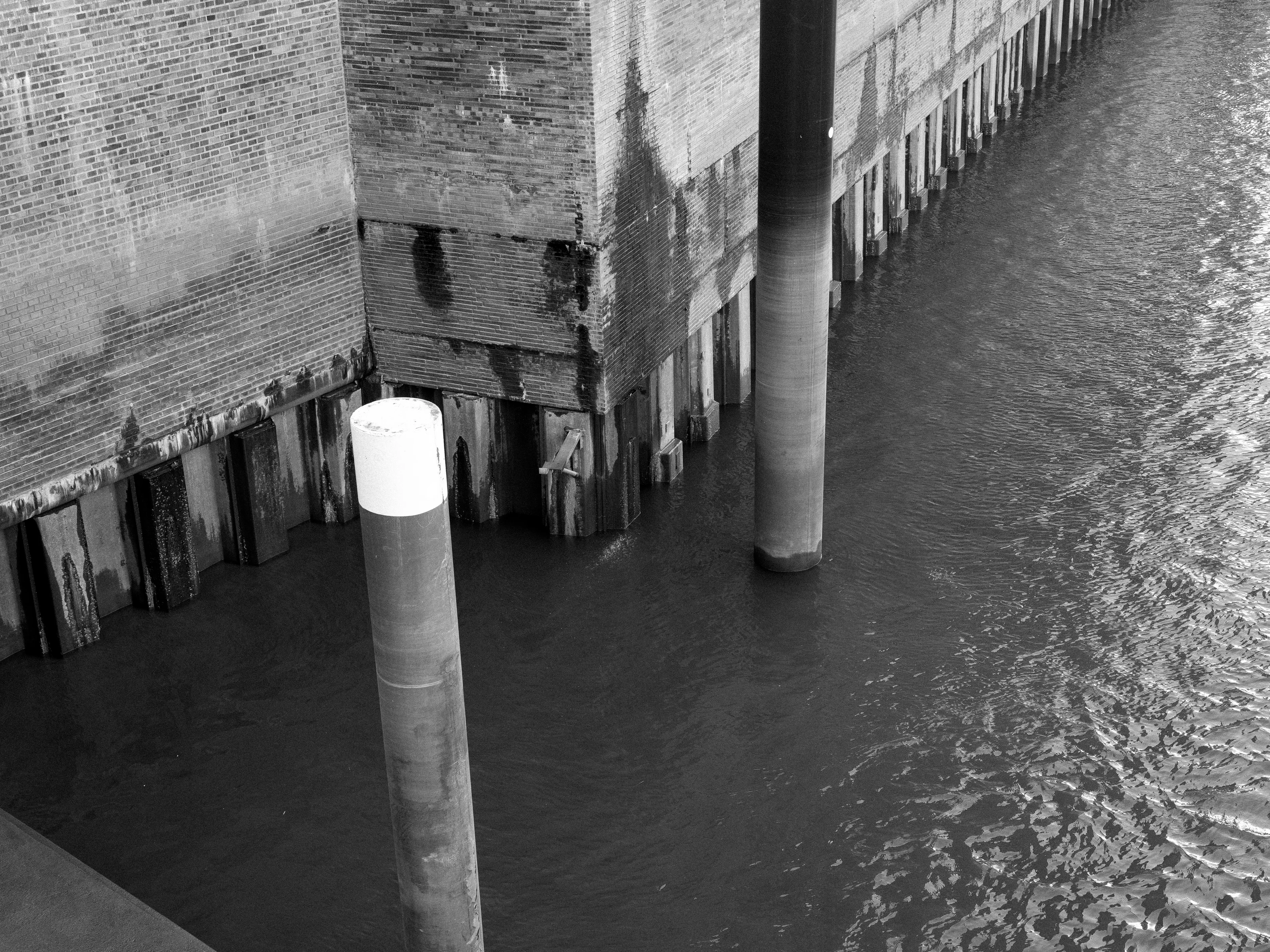 A black and white image of a brick wall with cylindrical pillars and water.