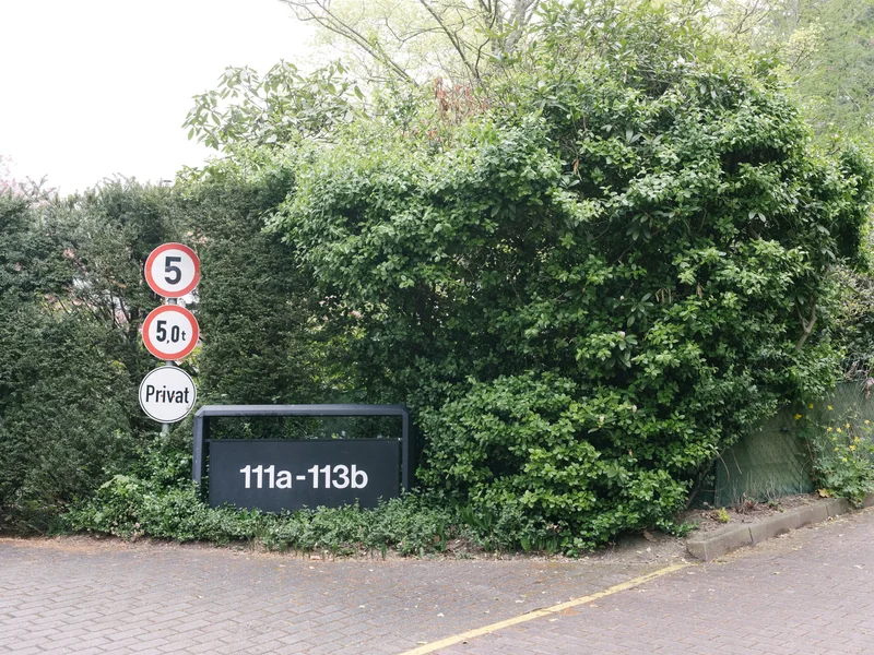 Safety signs and a location sign are placed beside dense greenery.