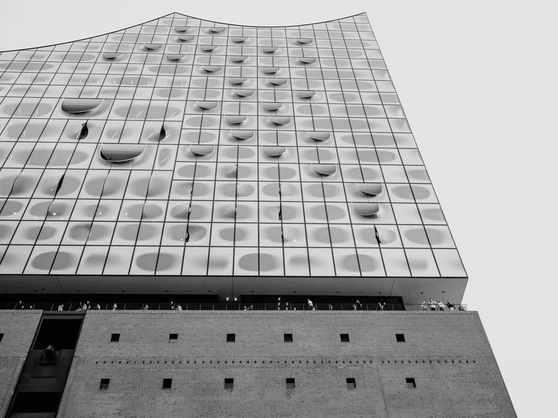 Black and white photo of a modern building facade with a wavy glass structure and brick base.