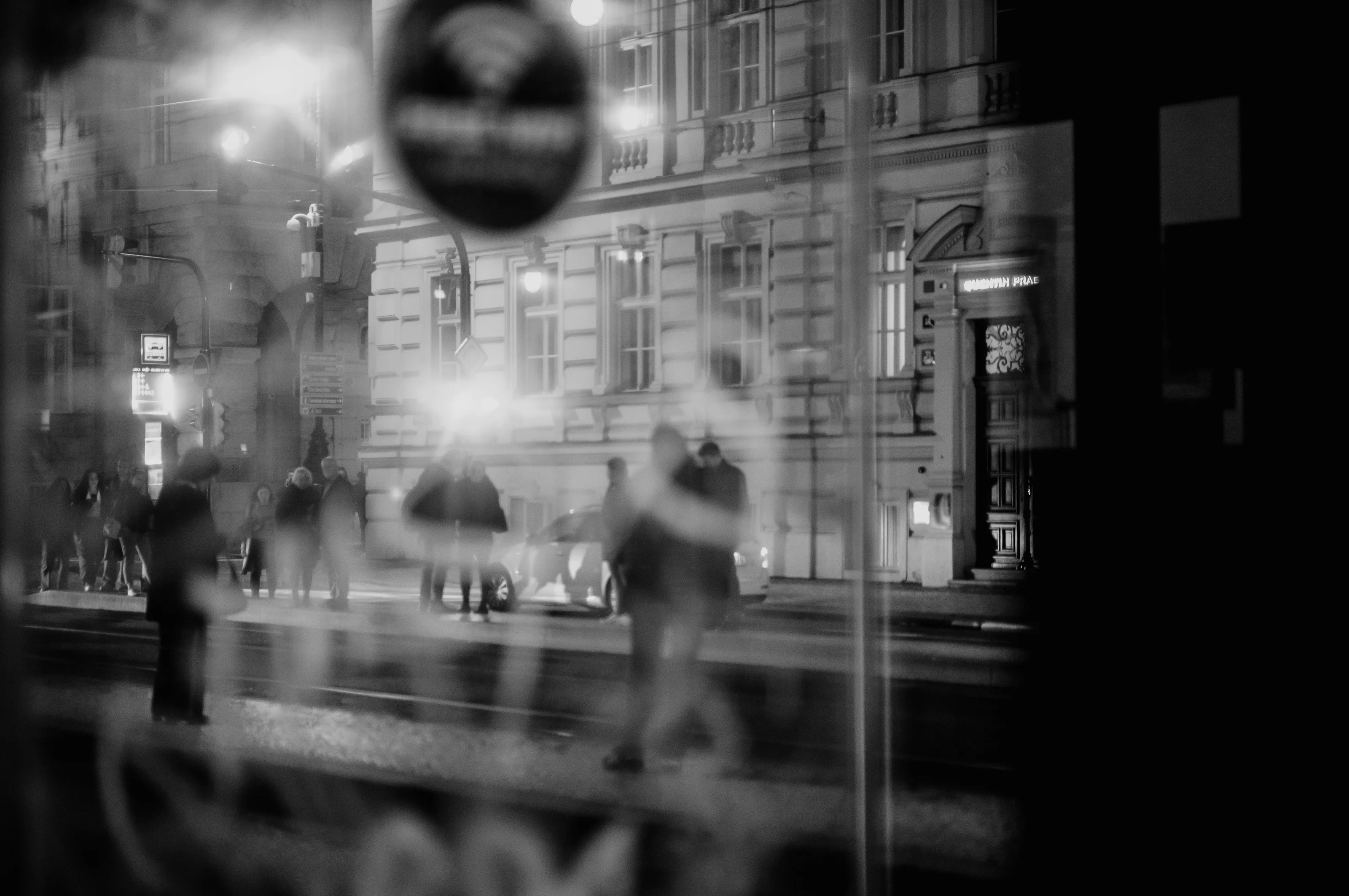 Blurry silhouette of people walking near a building at night.