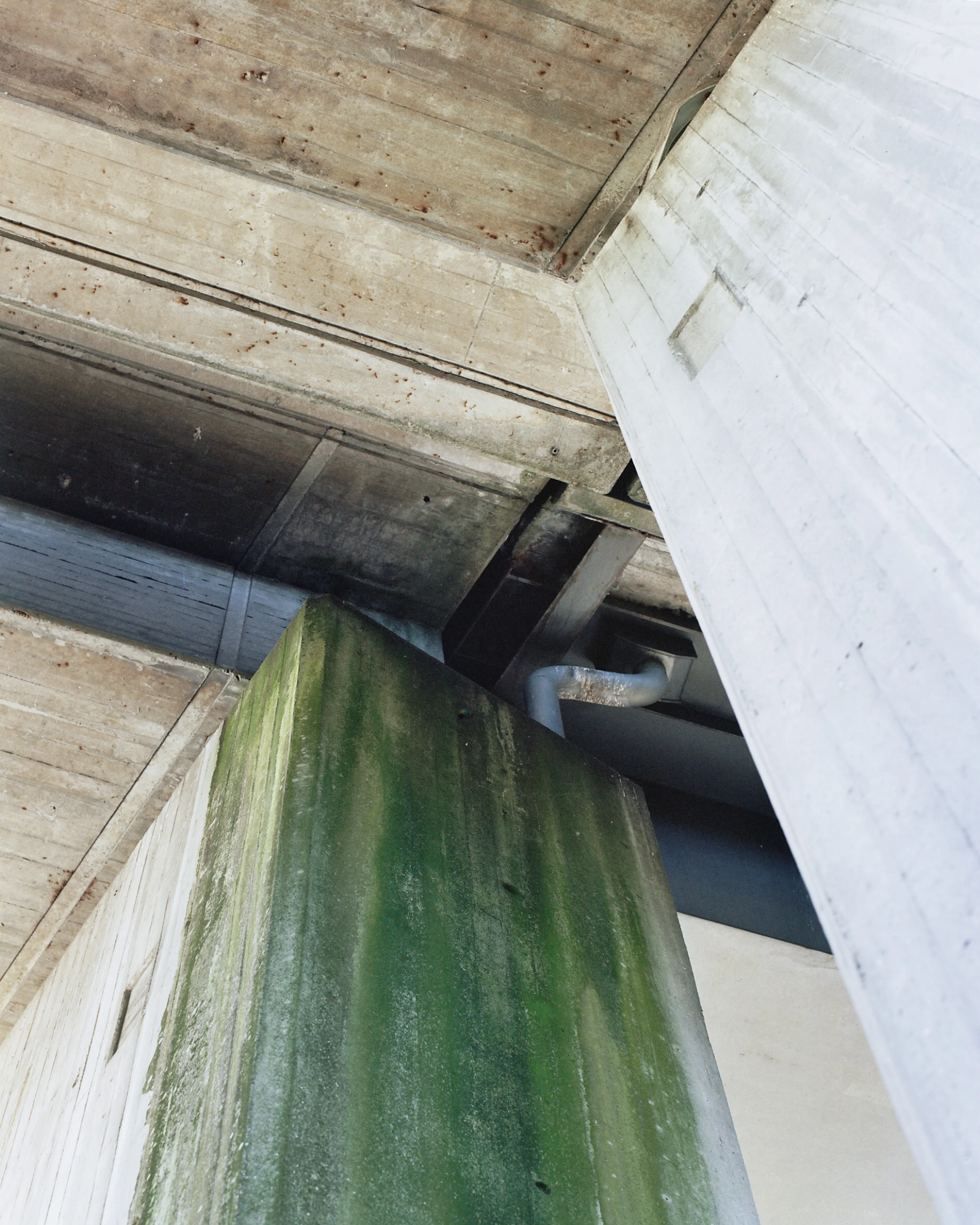Concrete architecture with a green-stained pillar and overhead beams.