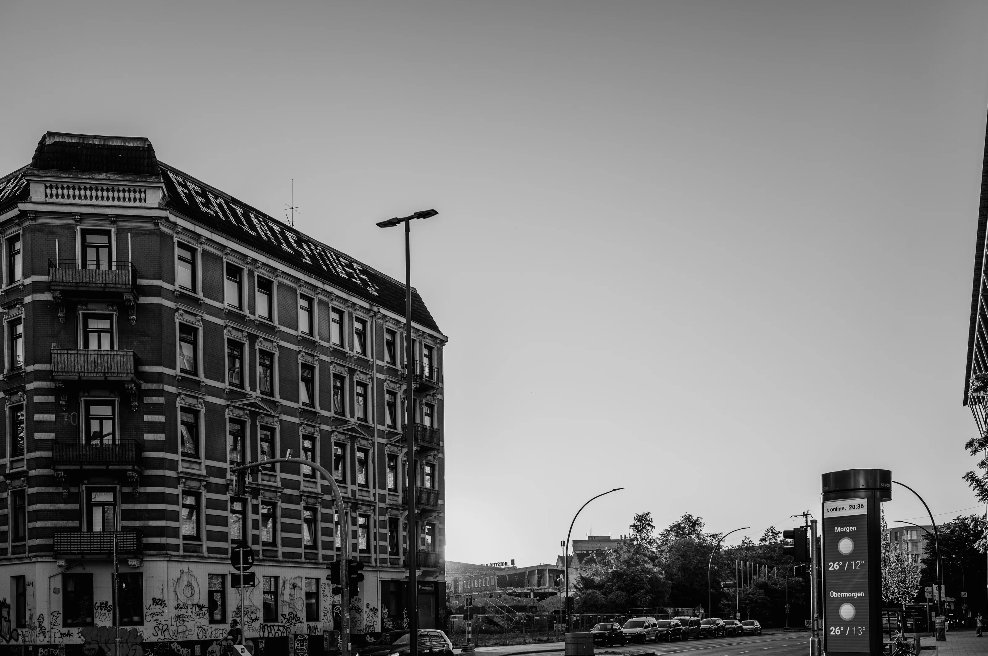 A multi-story building with graffiti at its base and a nearly empty street beside it under a clear sky.