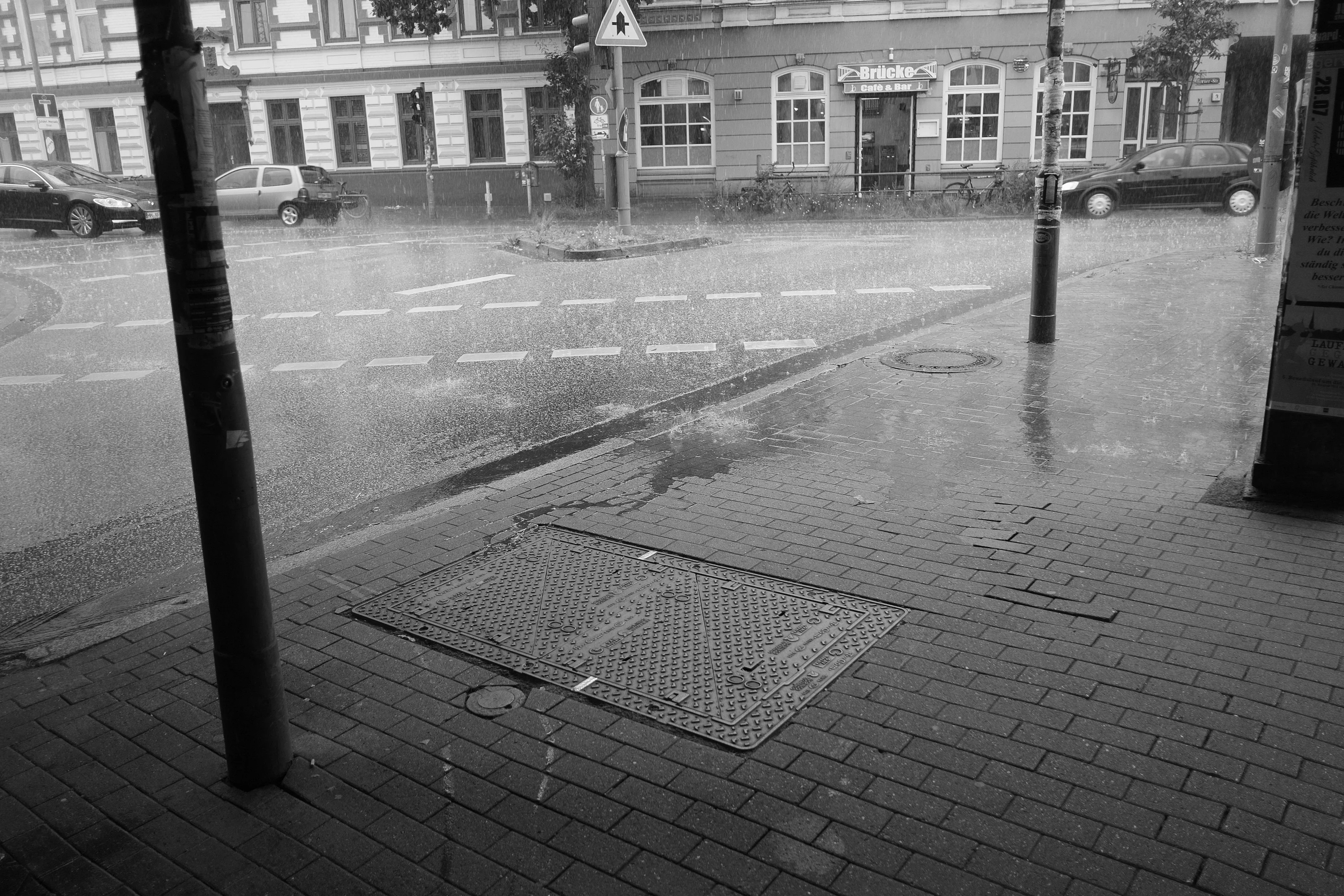 Street view of heavy rain pouring onto a city sidewalk and road intersection.