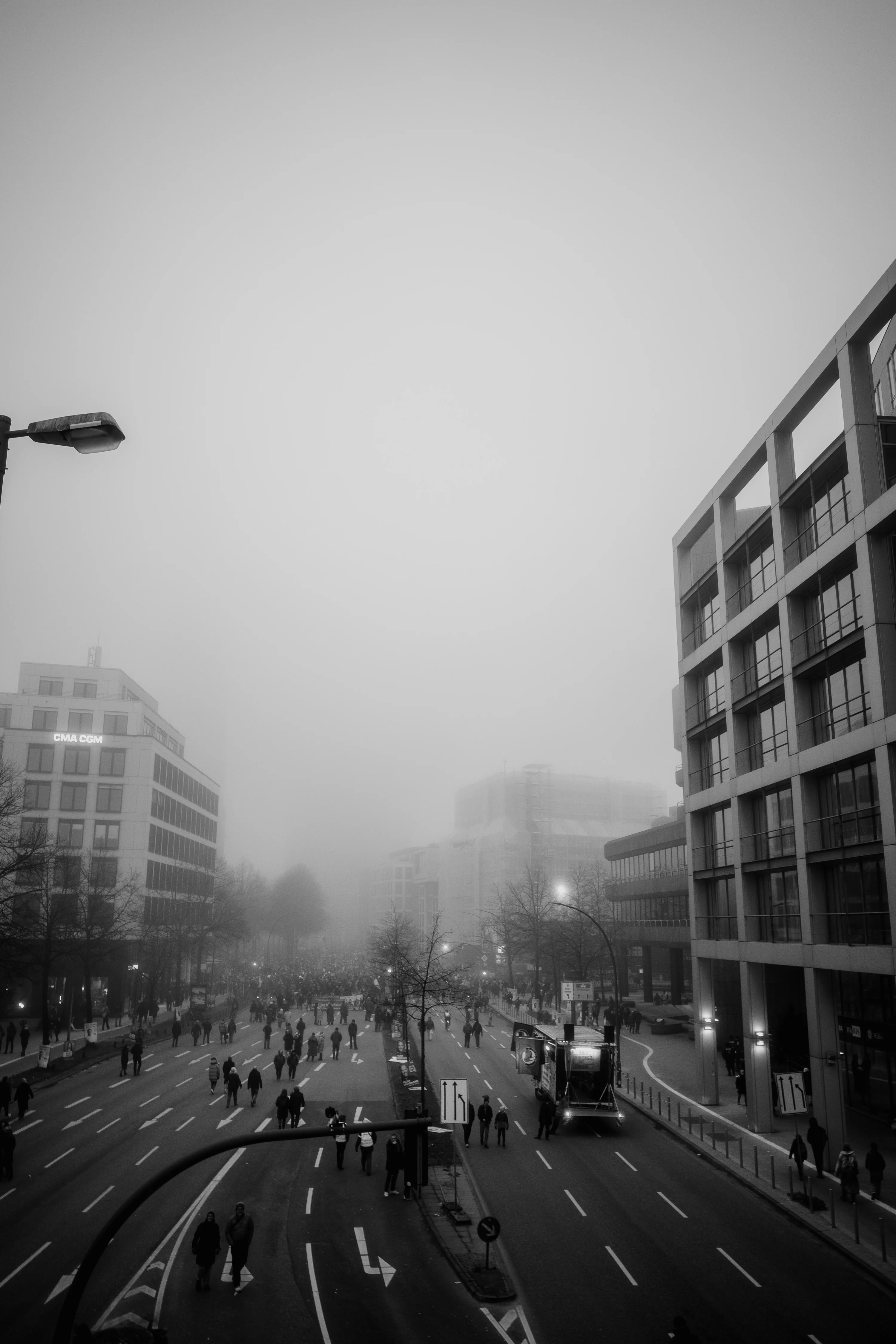 Black and white photo of a busy city street with people walking and buildings shrouded in fog.