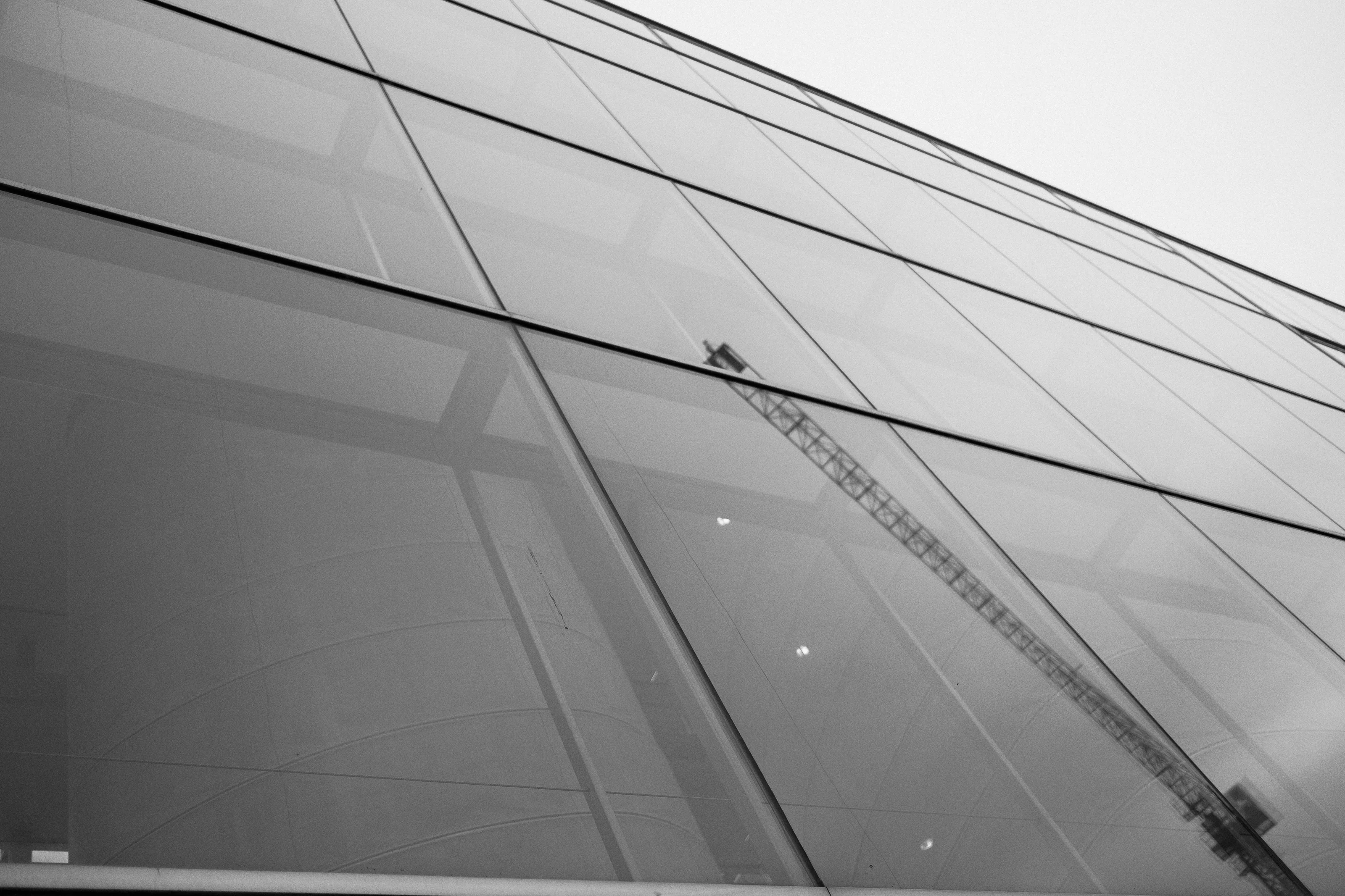 Black and white image of a modern glass building with a crane reflected on the facade.