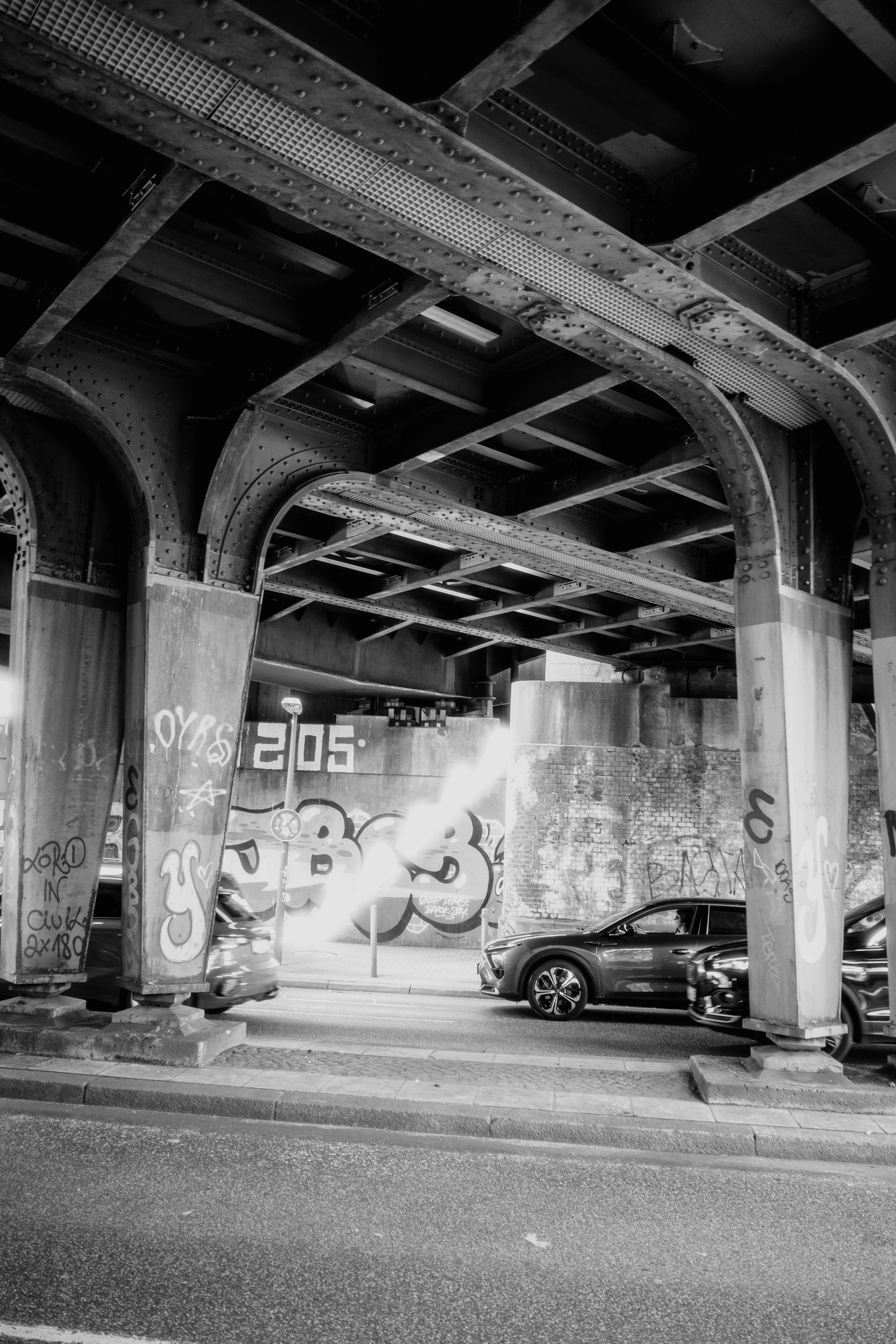 Black and white photo of graffiti-covered underpass with cars passing beneath.