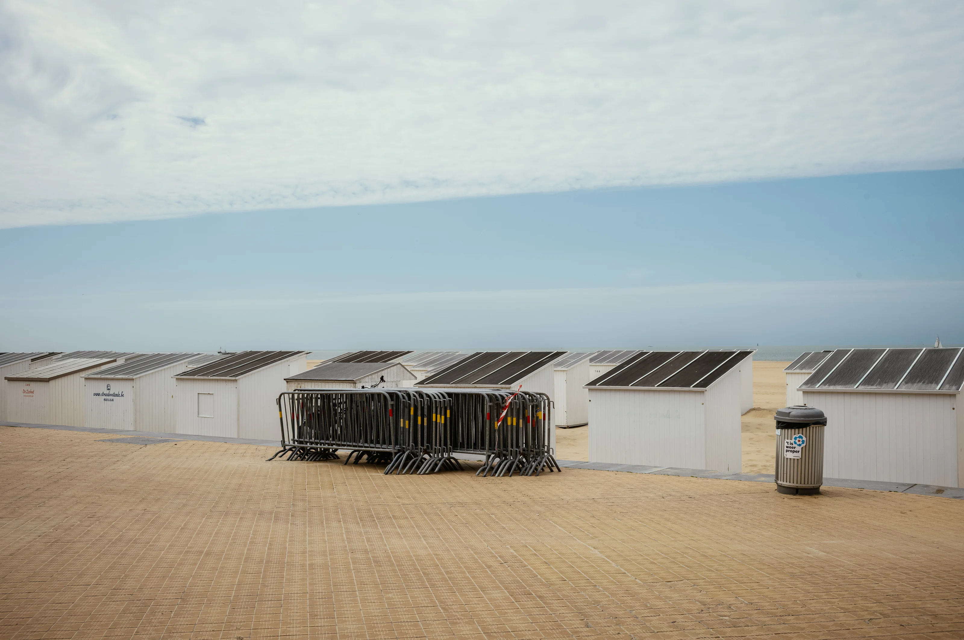 A sandy beach with several white cabins and metal barriers, under a partly cloudy sky.