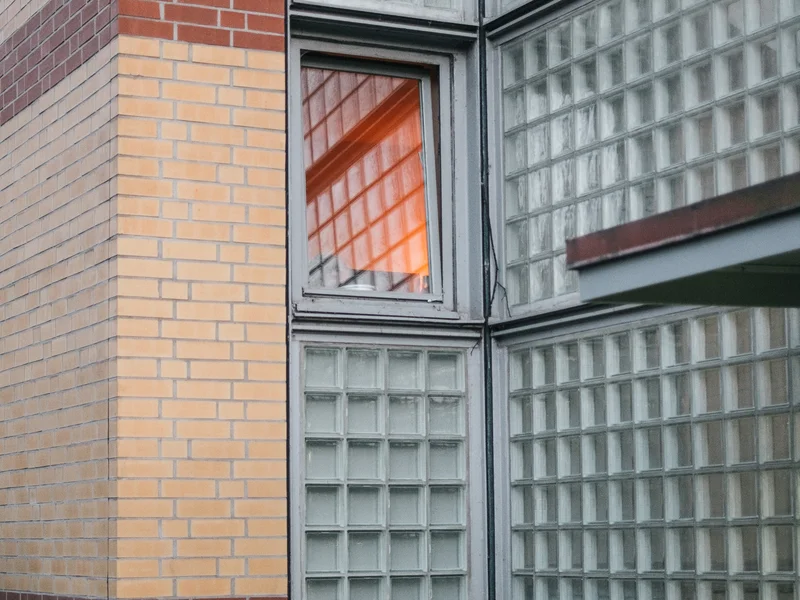 Bicycle parked against a building with a brick design and glass block windows reflecting orange light.