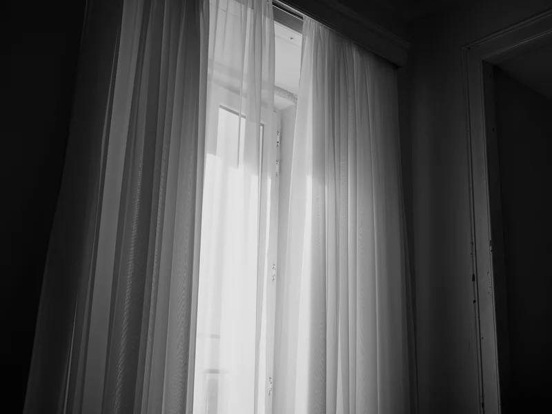 A softly lit window with sheer curtains partially open, letting light in.