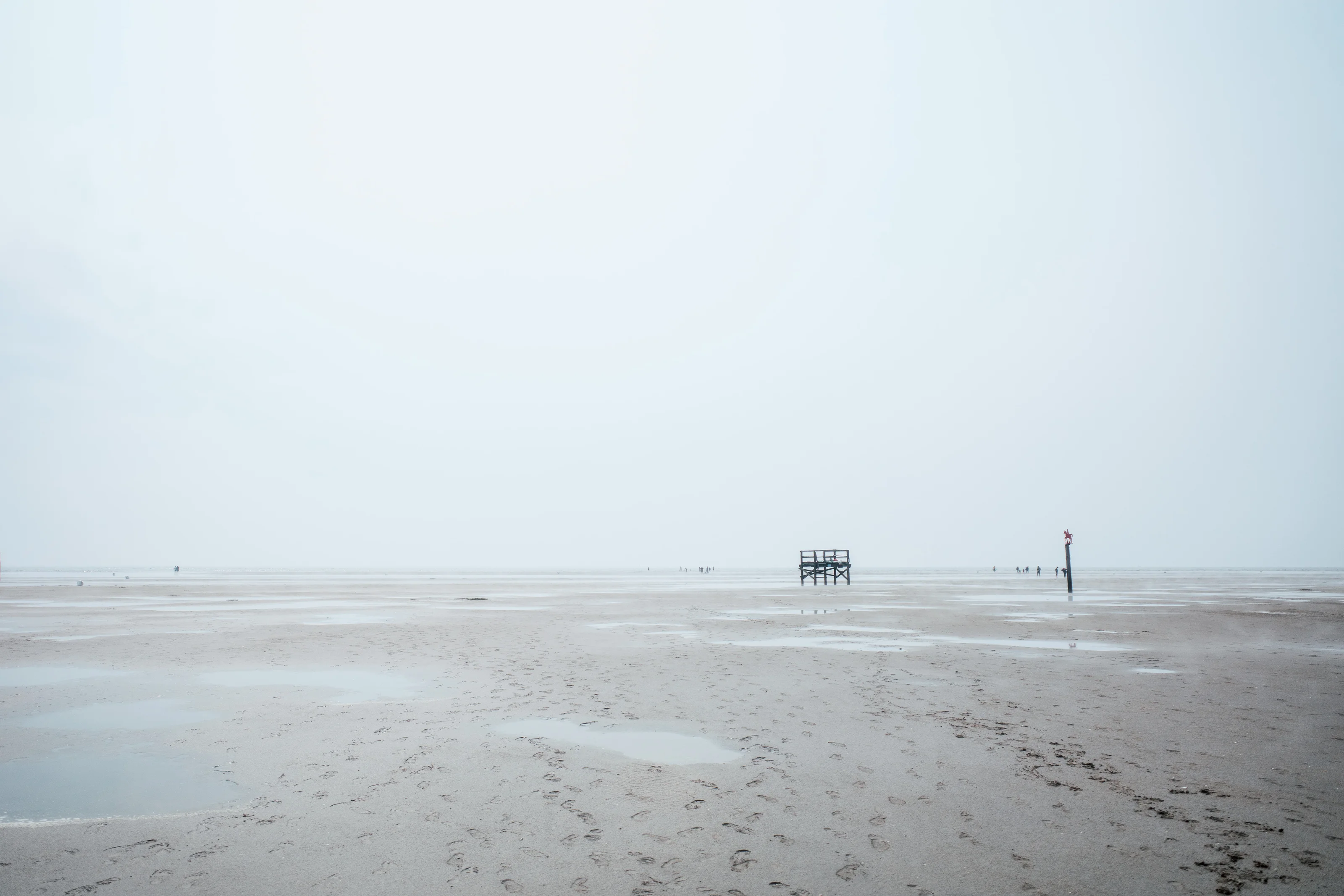 A vast, empty beach with a distant lifeguard stand and calm ocean in the background.