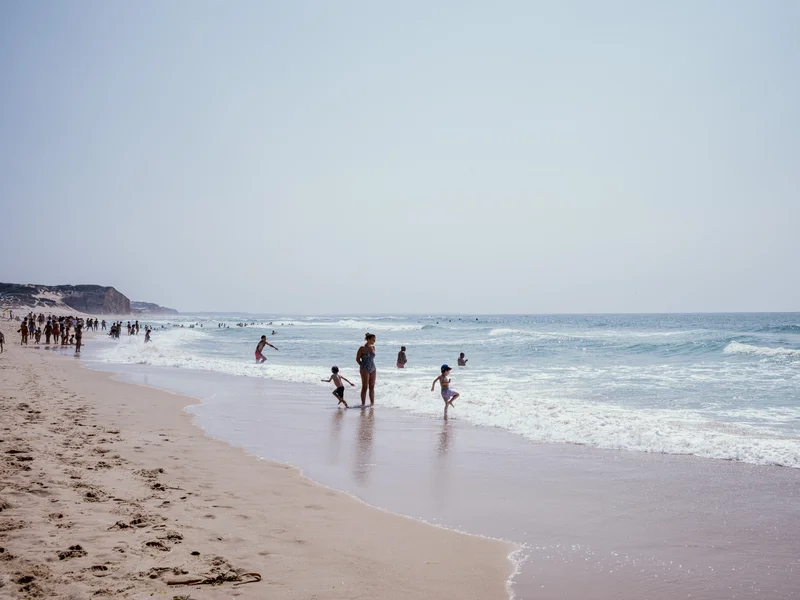People enjoying a sunny day at the beach with waves in the background.