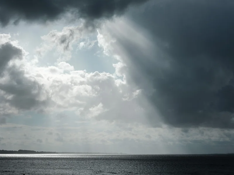 Sun rays breaking through dark clouds over a calm sea.