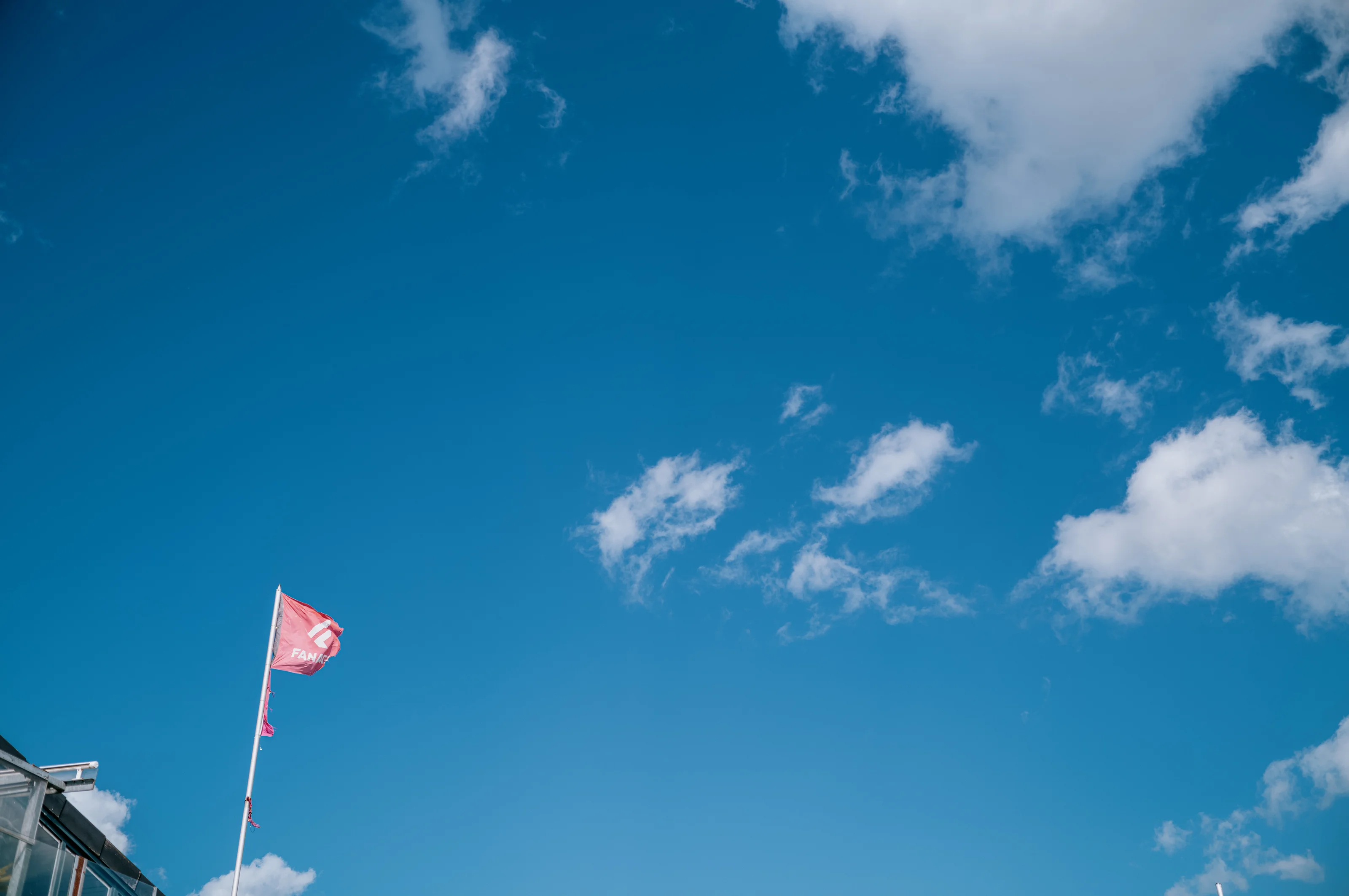 A red flag flying against a clear blue sky with scattered clouds.