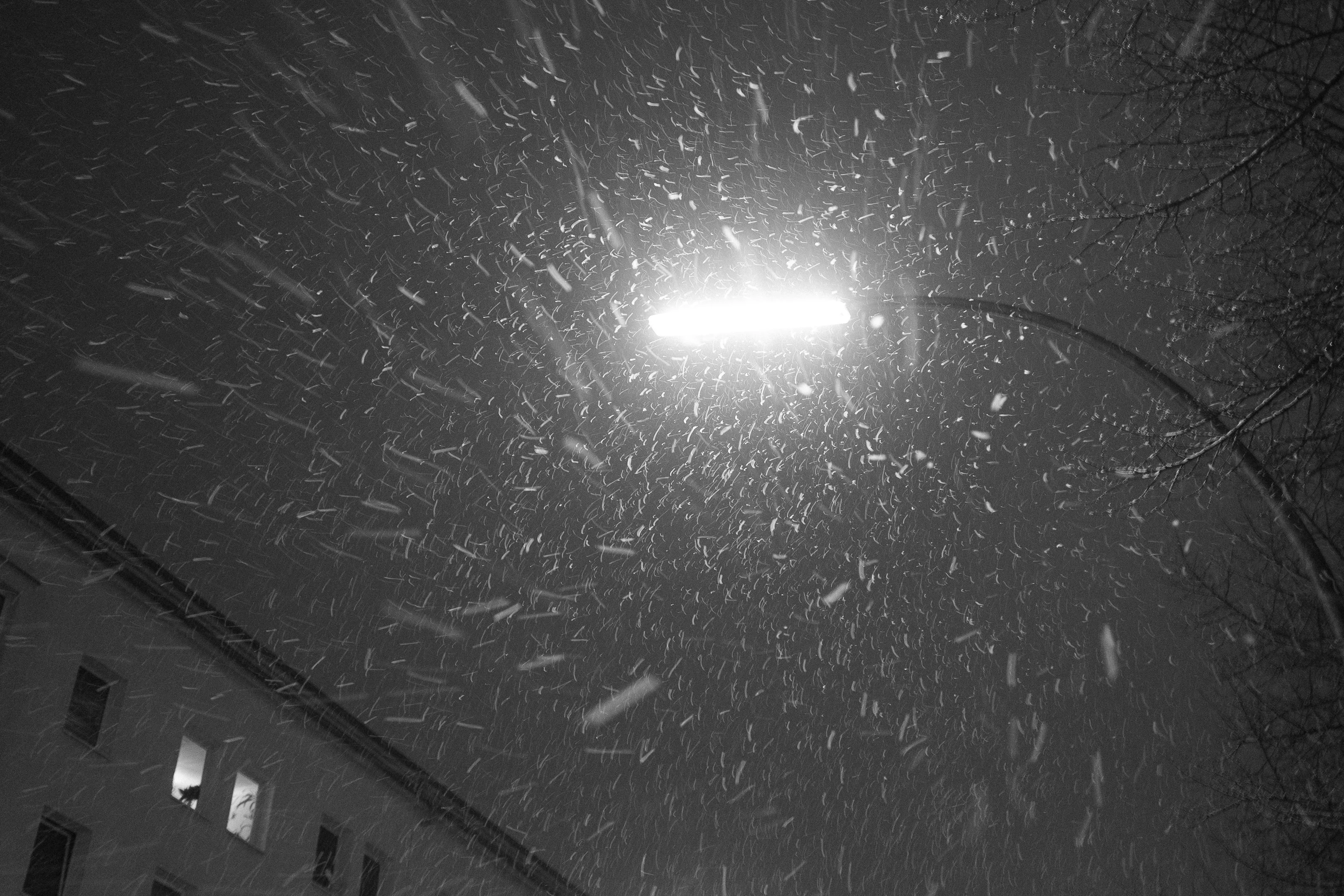 A streetlight illuminates falling snowflakes at night next to a building.