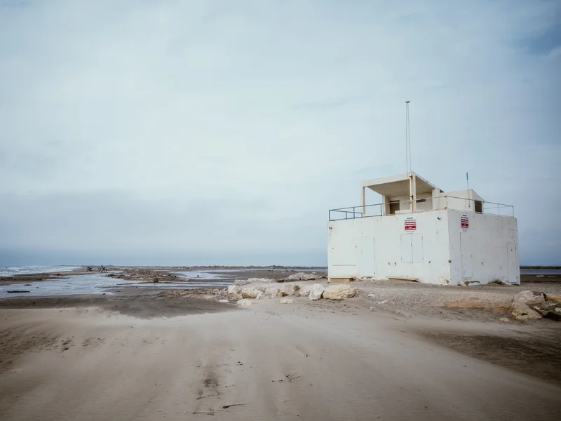 A white lifeguard tower stands on a deserted beach with overcast skies.