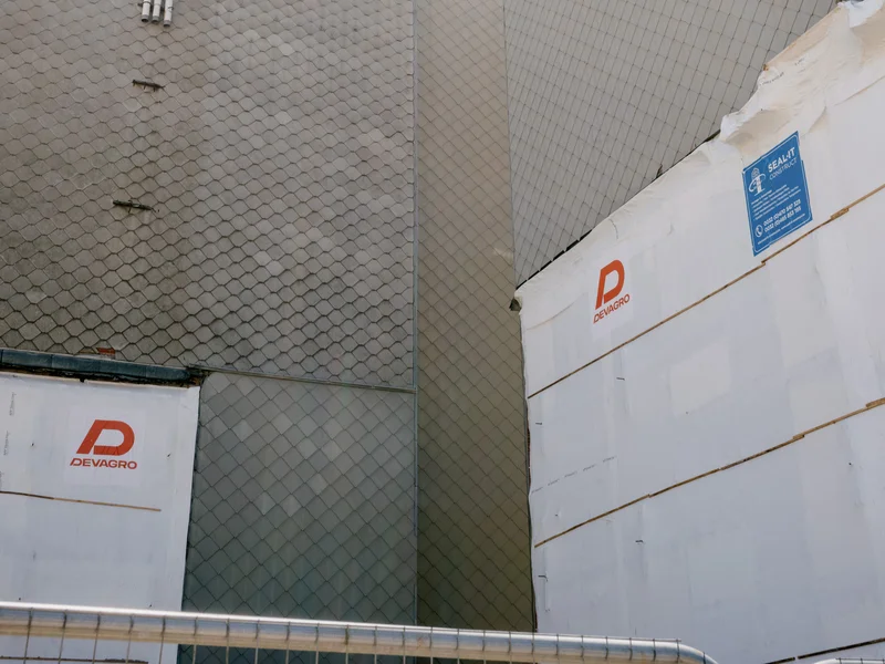 Tall gray tiled buildings with construction signs under a partly cloudy sky.