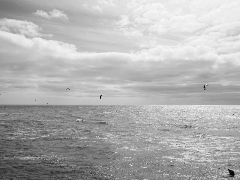 Several kitesurfers on a vast ocean under a cloudy sky.