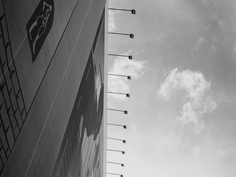 Side view of a large building with wall lamps extending outward, against a cloudy sky.