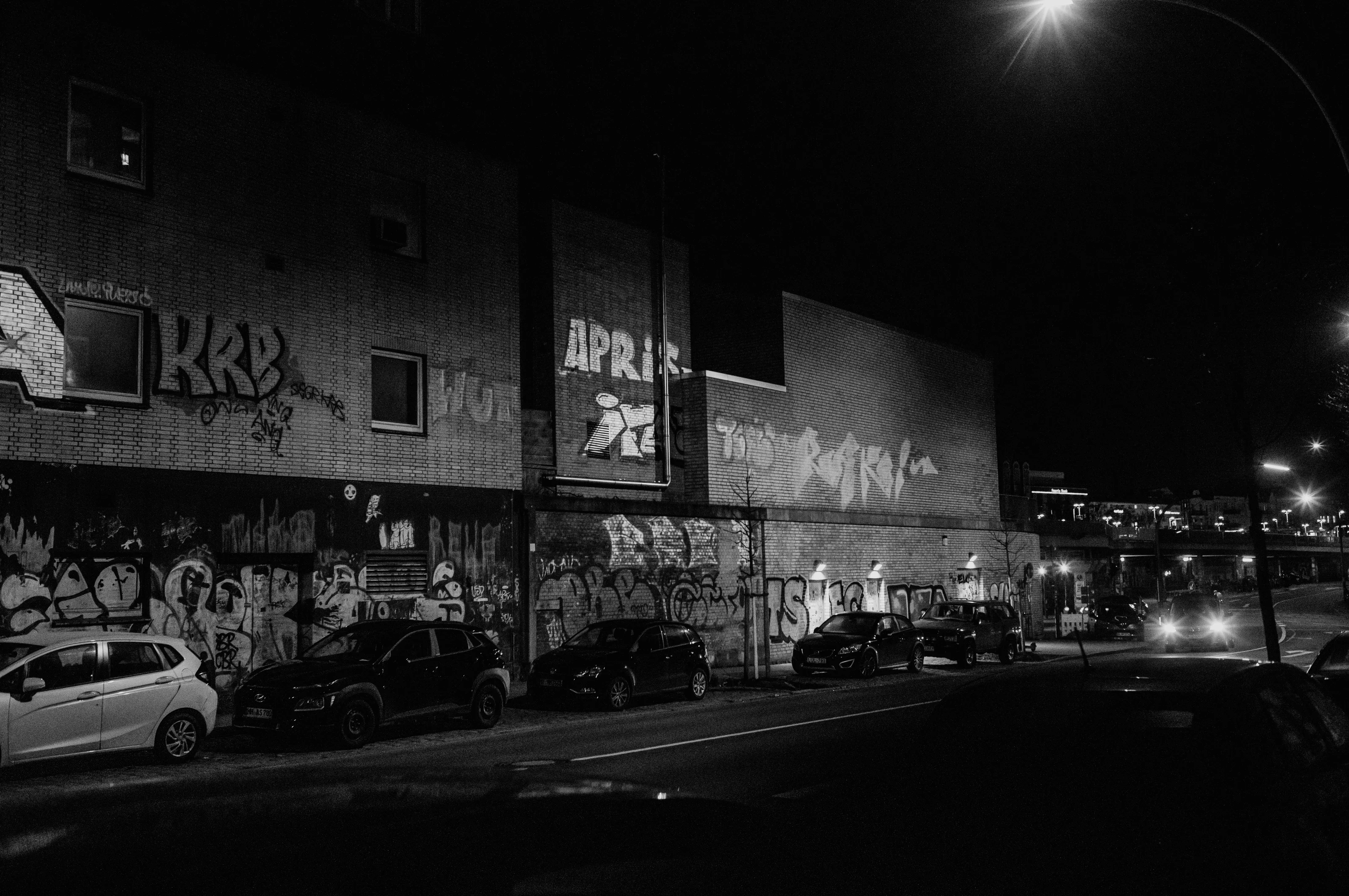 Nighttime street scene with graffiti-covered building and parked cars.