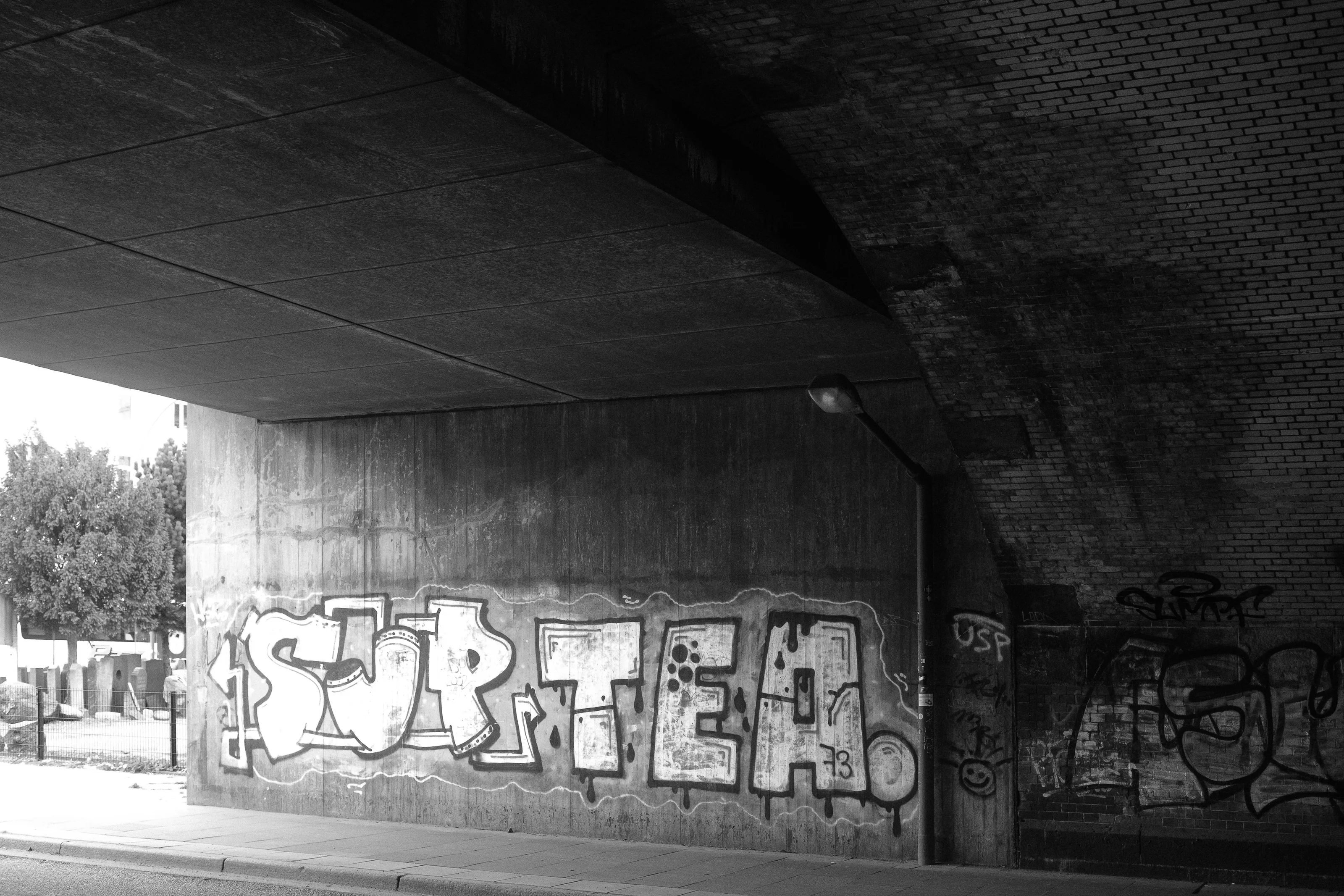 Black and white photo of graffiti under an overpass.