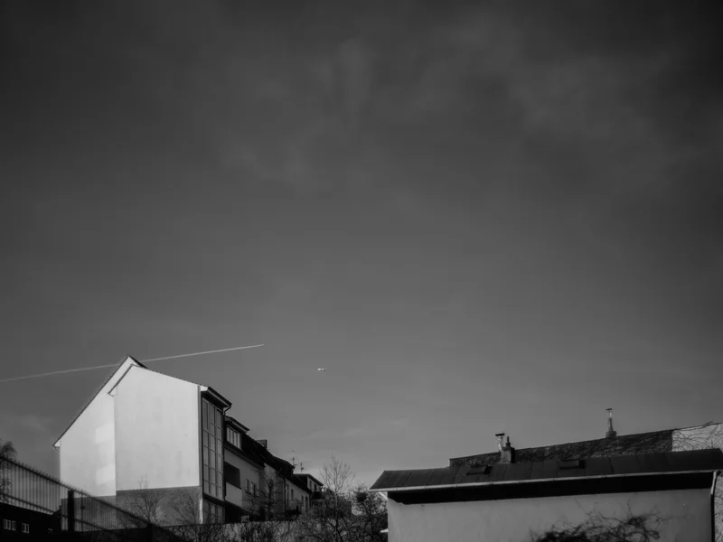 A minimalist cityscape with a contrail and small airplane above a building.