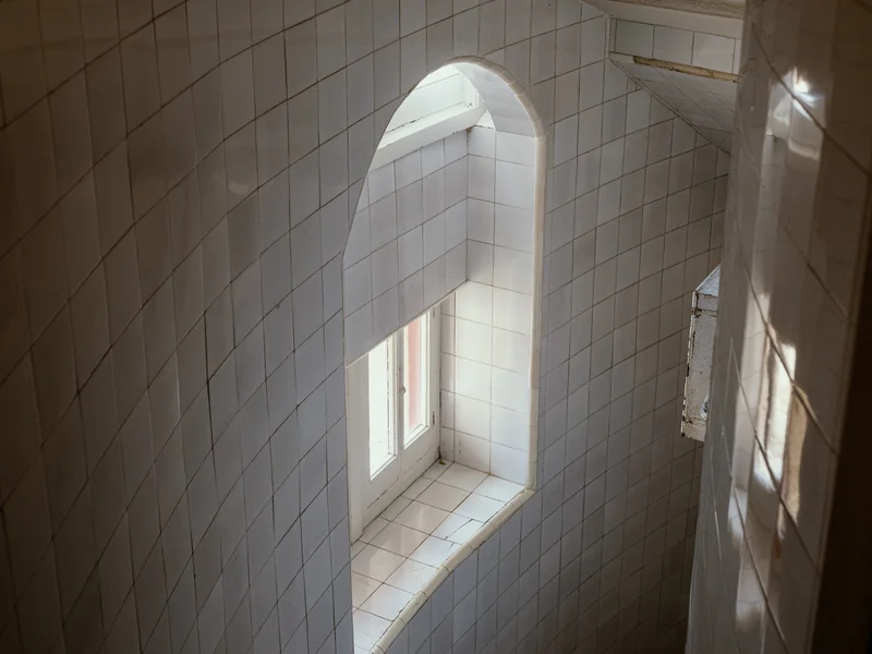 A spiral staircase with tiled walls and a window at the landing.
