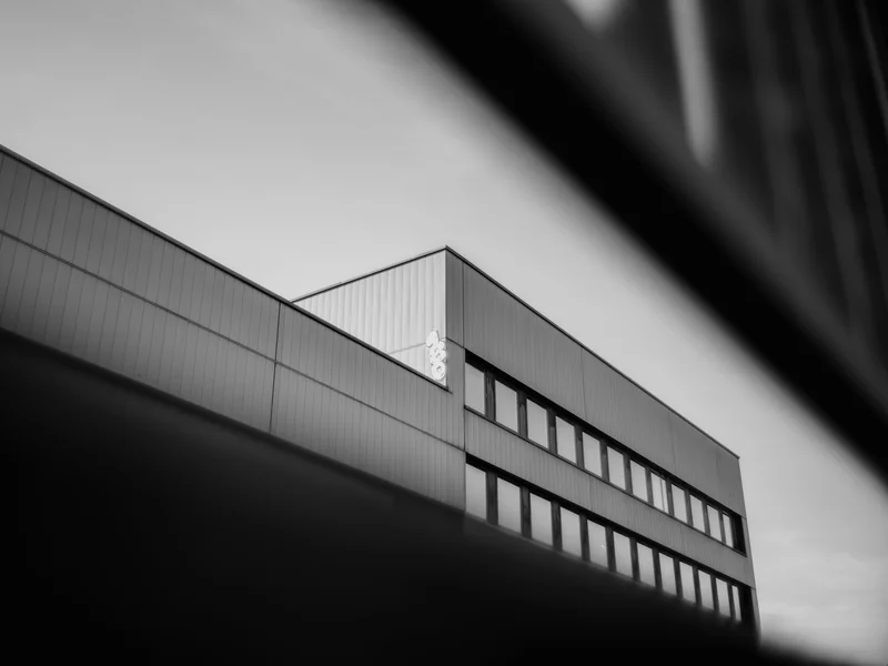 Black and white image of a modern building with multiple large windows and a partially visible sign.