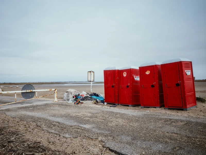 Red portable toilets next to a pile of trash on a deserted landscape.