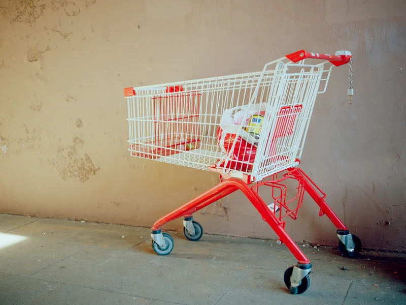 A red and white shopping cart filled with items against a textured wall.