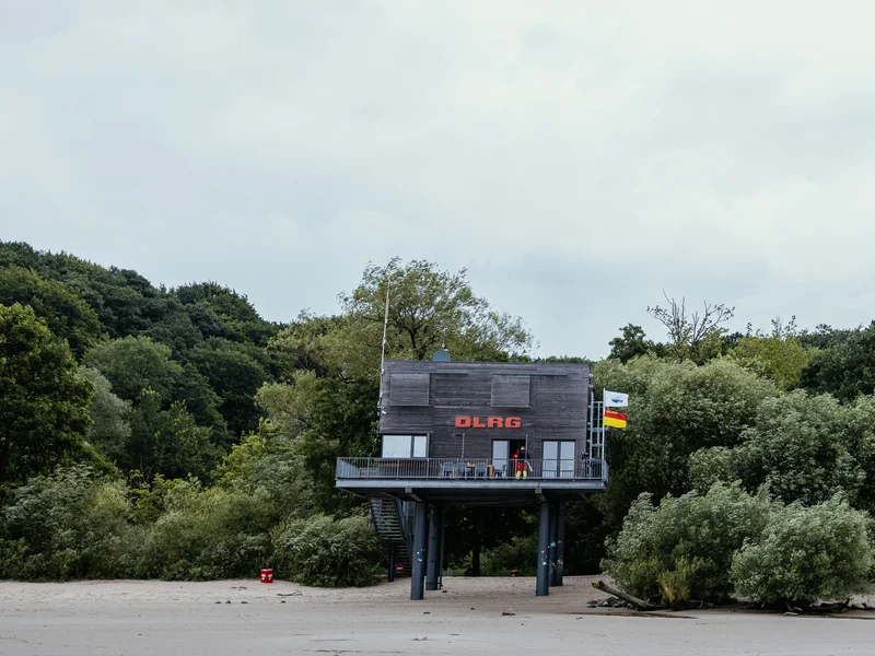 A lifeguard station on stilts near a beach, surrounded by trees.