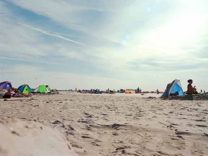 People relaxing under tents on a sandy beach with a bright sky overhead.