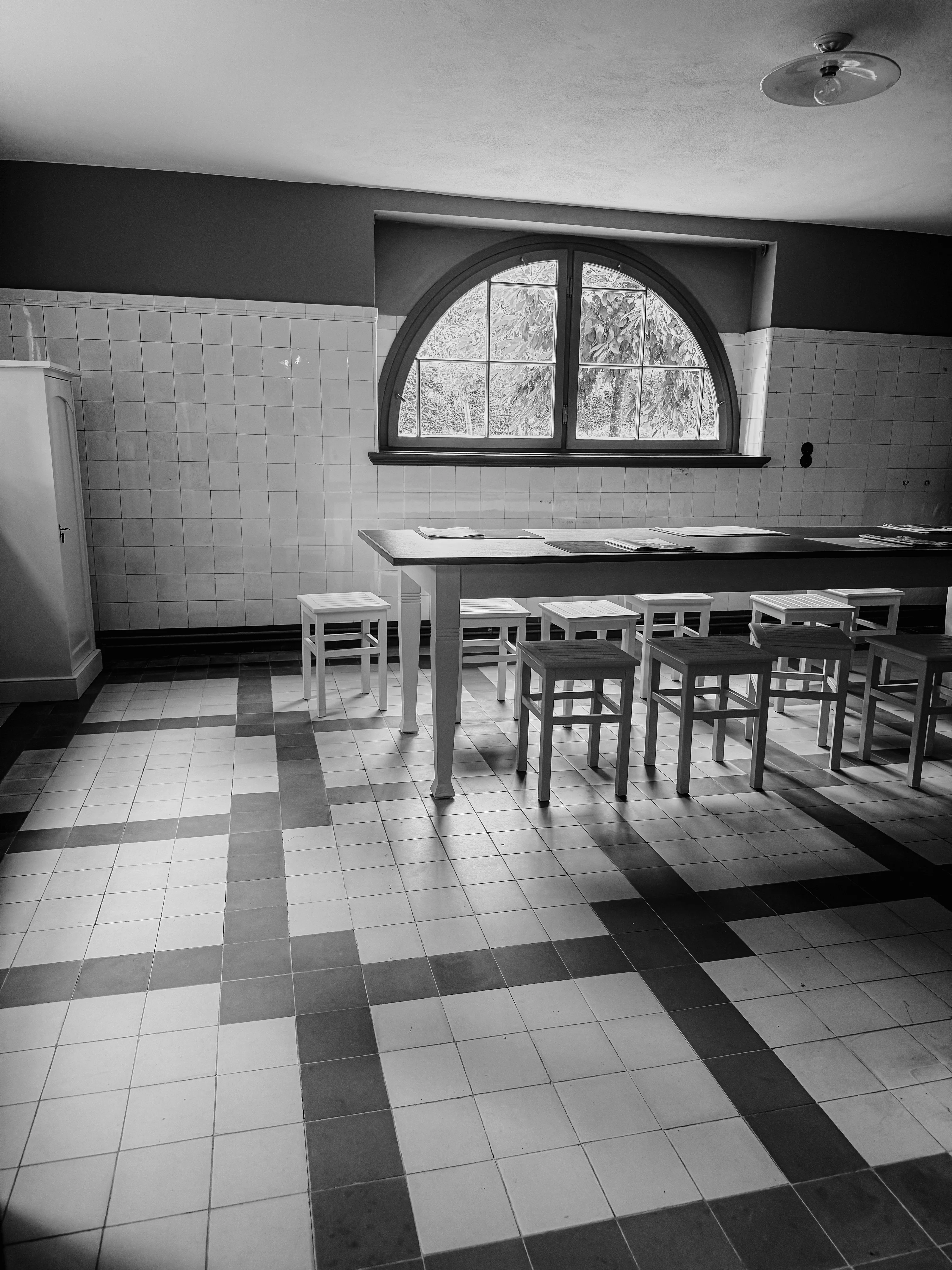 Black and white photo of a tiled room with a window, table, and stools.