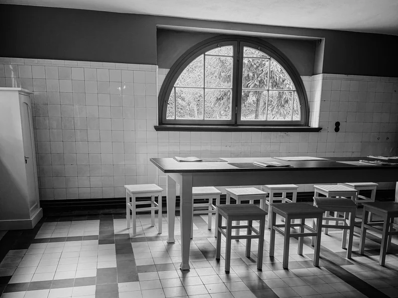 Black and white photo of a tiled room with a window, table, and stools.